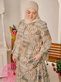 A woman wearing a beige hijab and a long-sleeved, patterned maxi abaya with pockets, standing in a softly lit indoor setting with a wooden bench and pink flowers.