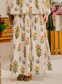 A person wearing a cream-colored two-piece set with a colorful floral print, consisting of a ruffled long-sleeve top and a matching tiered maxi skirt, paired with brown sandals.