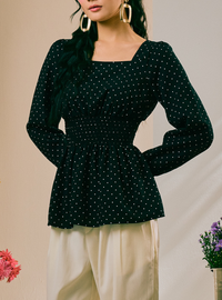 A woman wearing a dark green long-sleeve top with a white polka dot pattern and a square neckline, paired with cream-colored pants.