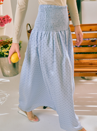 A person wearing a light blue high-waisted maxi skirt with a small black polka dot pattern and a smocked waistband, paired with a beige long-sleeve top and clear slide sandals.