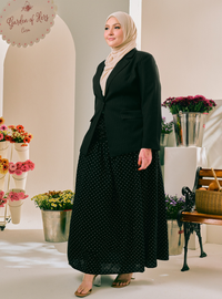 A woman wearing a black blazer, a black maxi skirt with white polka dots, and a light beige hijab stands in a boutique setting with floral arrangements and a sign that reads 'Garden of Her'.