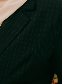 Close-up of a dark green pinstripe blazer with a beige sheer drape and a small green ring detail visible at the bottom right.