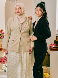 Two women posing together in coordinated professional outfits. The woman on the left wears a beige blazer and matching hijab over a cream polka-dot dress.
