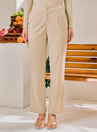 A person wearing beige wide-leg cropped pants with a matching long-sleeve top and clear heeled sandals, standing indoors near a wooden bench and fruit display.